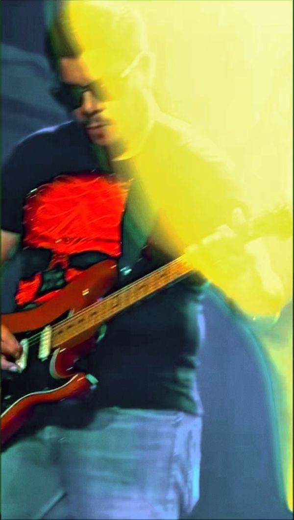 Guitarist playing a red electric guitar, blurred by yellow stage light